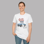 A man wearing a white graphic t-shirt with a vintage-style print of an Austin Healey 3000 sports car, paired with blue jeans, set against a solid gray background.
