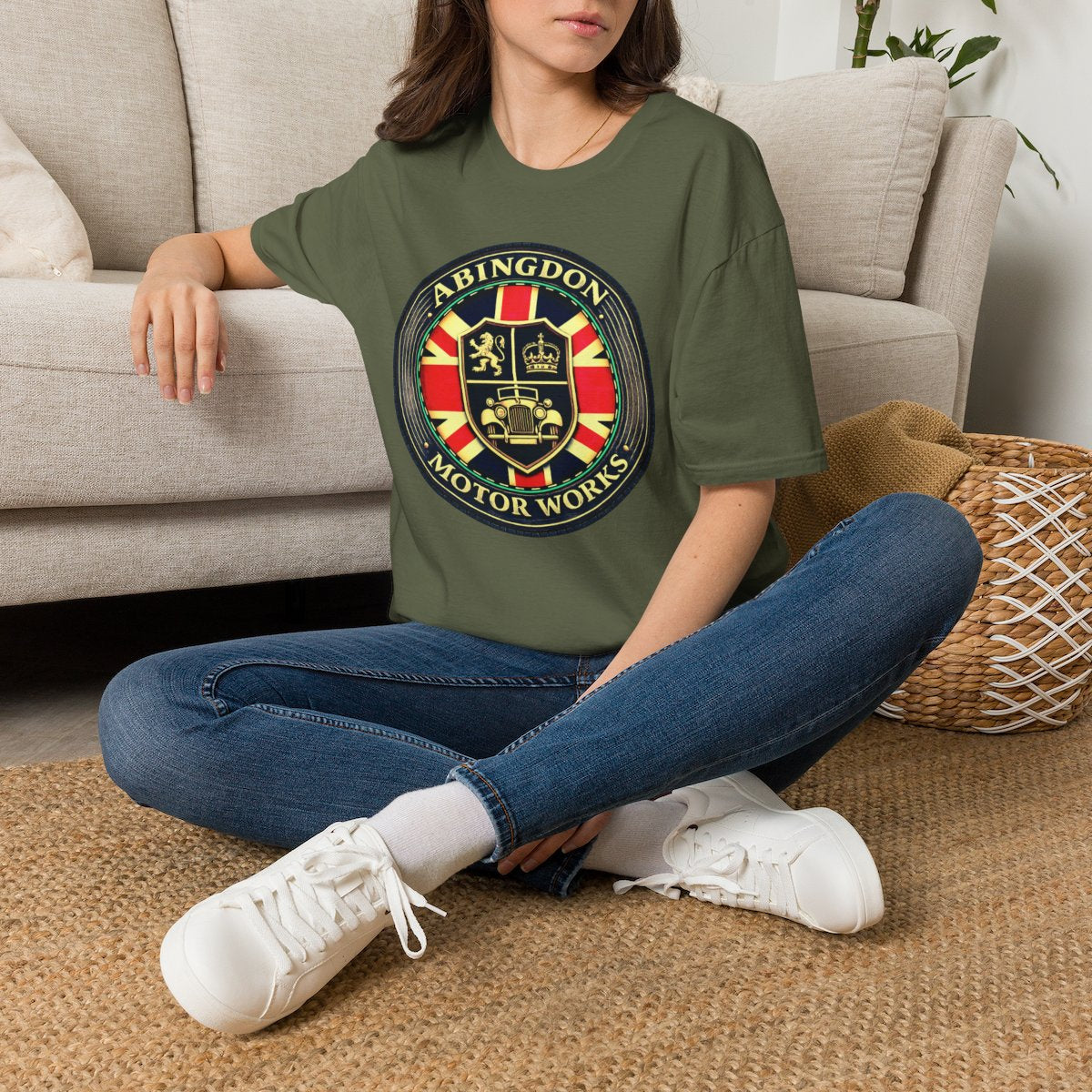 Person wearing a military green t-shirt with a circular 'Abingdon Motor Works' crest printed on the chest sitting on the floor.