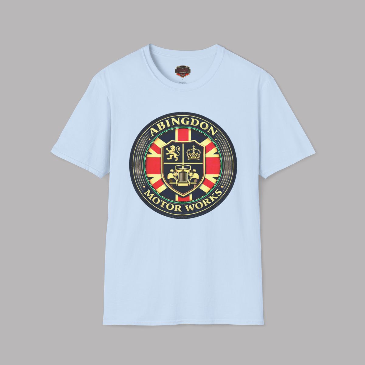 A light blue short-sleeve crewneck t-shirt featuring a large circular 'Abingdon Motor Works' crest graphic printed on the chest, displayed against a solid gray background.