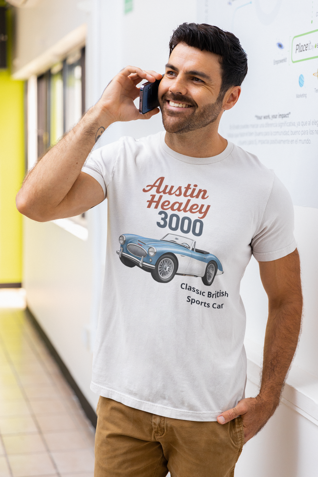 Man wearing a white t-shirt with an Austin Healey 3000 graphic, talking on a phone.