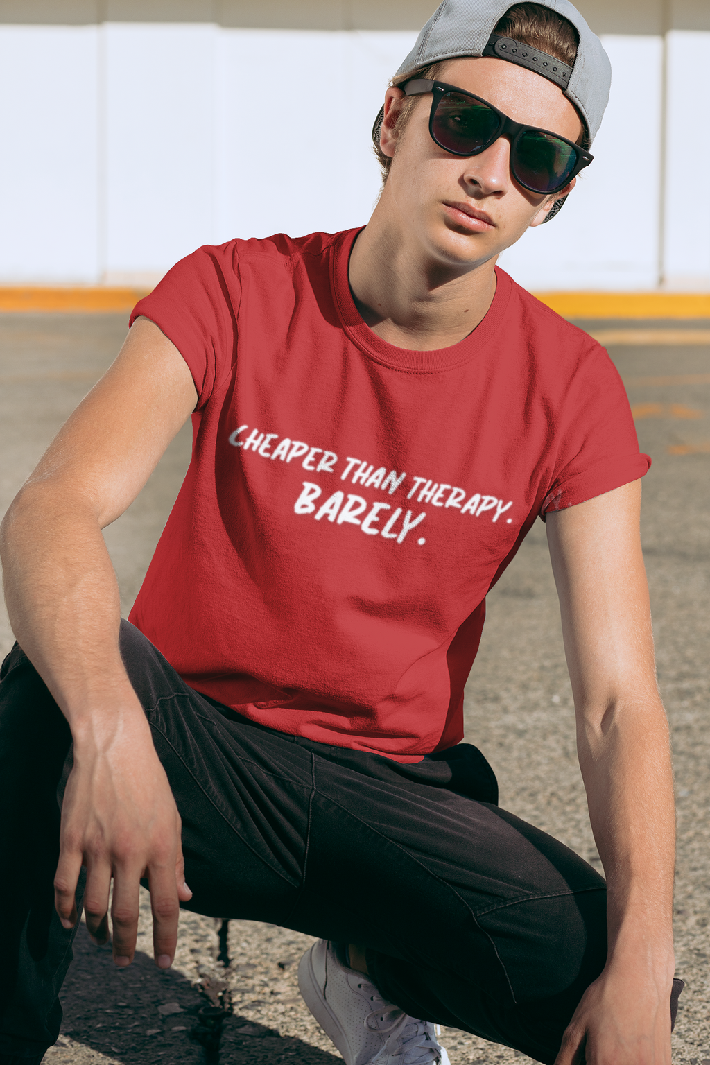Man wearing a red t-shirt with text 'Cheaper than therapy. Barely.' outside.