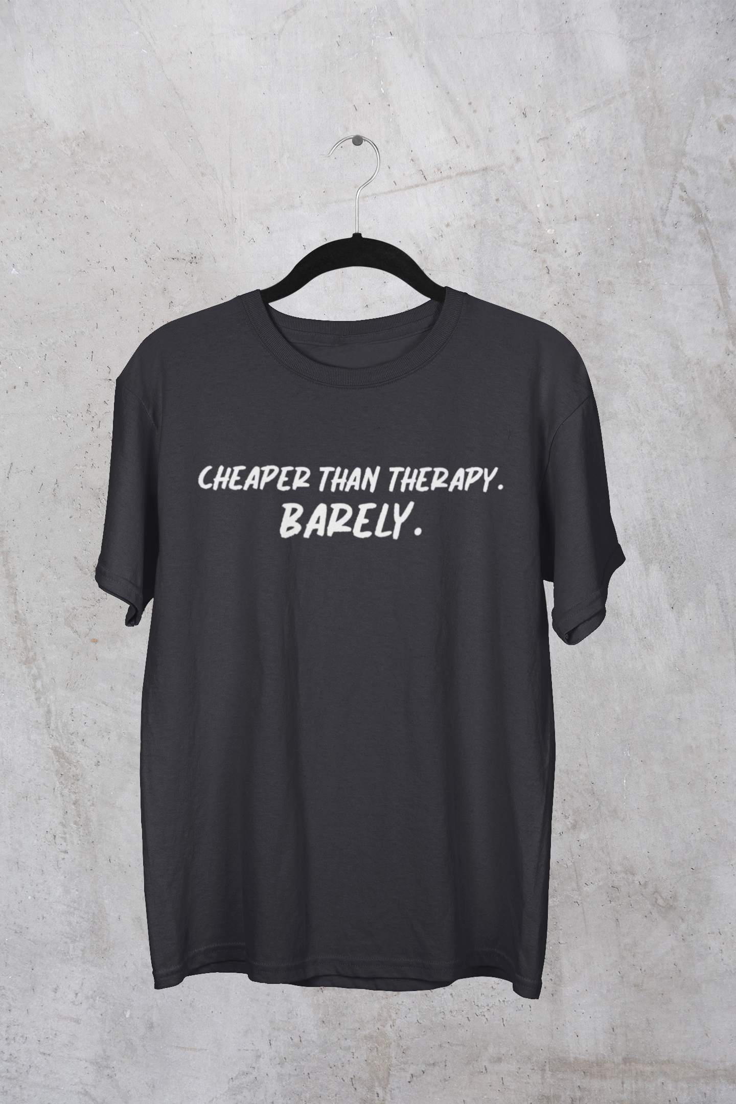 Dark heather t-shirt with white "Cheaper than Therapy. Barely. text on a hanger against a concrete wall background