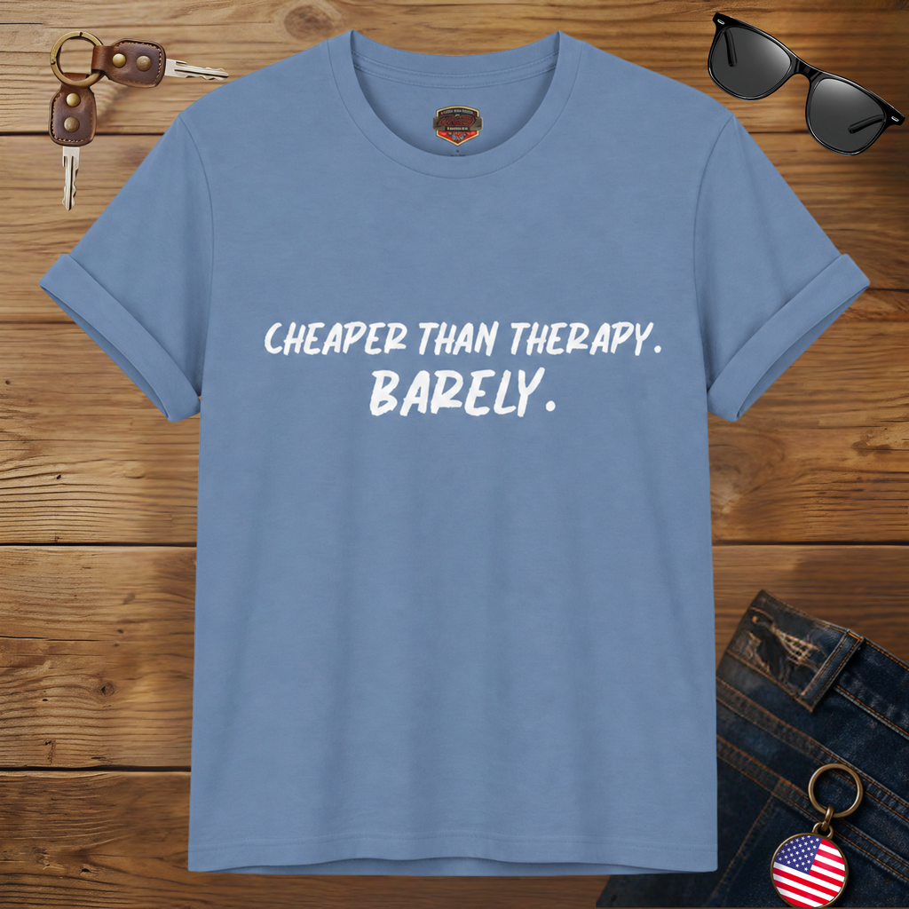 Steel blue t-shirt with text 'Cheaper than therapy. Barely.' on a wooden surface with sunglasses and keys.