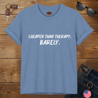 Steel blue t-shirt with text 'Cheaper than therapy. Barely.' on a wooden surface with sunglasses and keys.