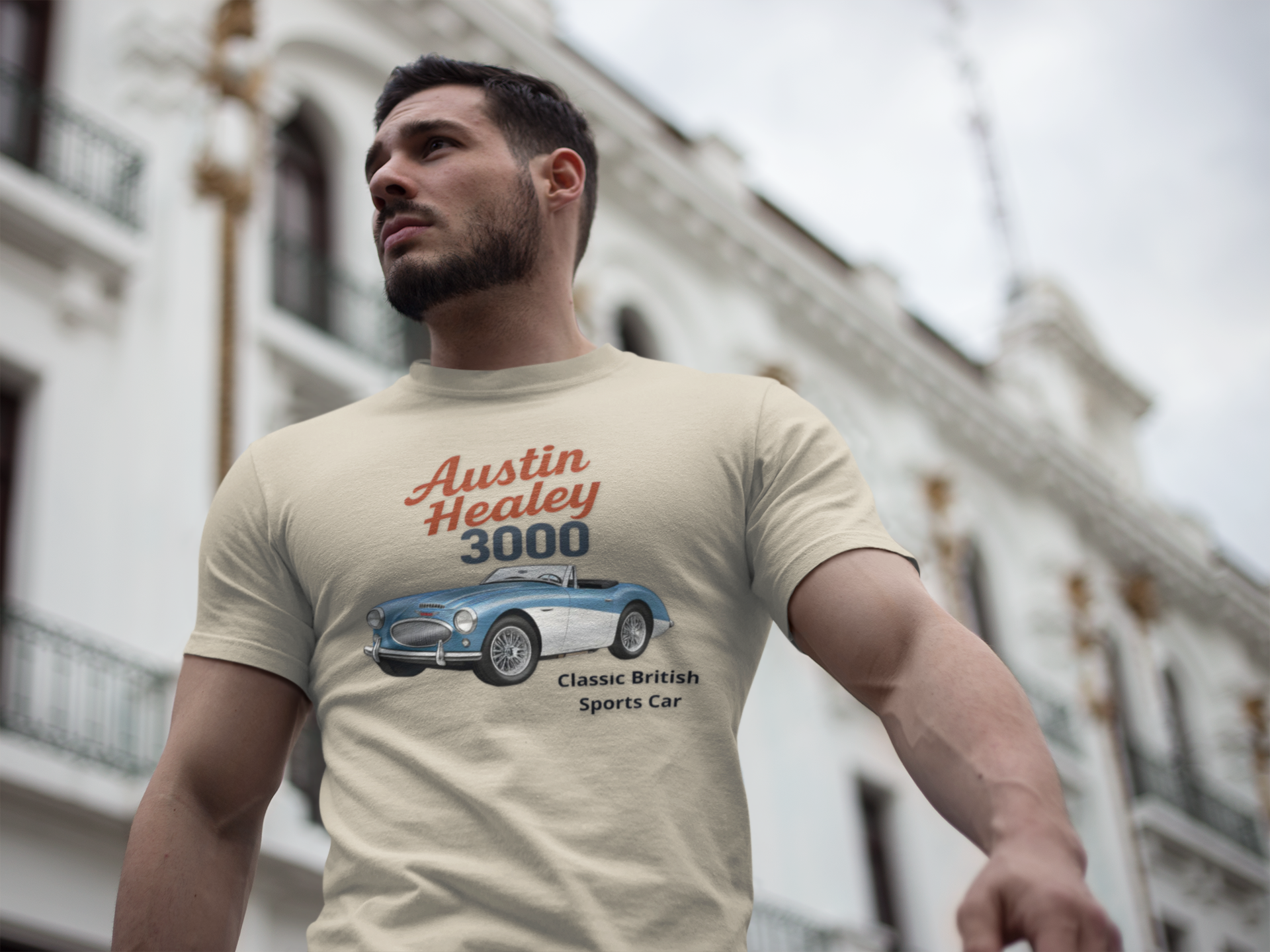 Man wearing a sand t-shirt with an Austin Healey 3000 graphic in front of a building.